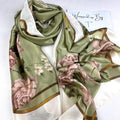 Sage green silk-satin scarf featuring large blush pink peonies and small white flowers with a gold and white bordered edge